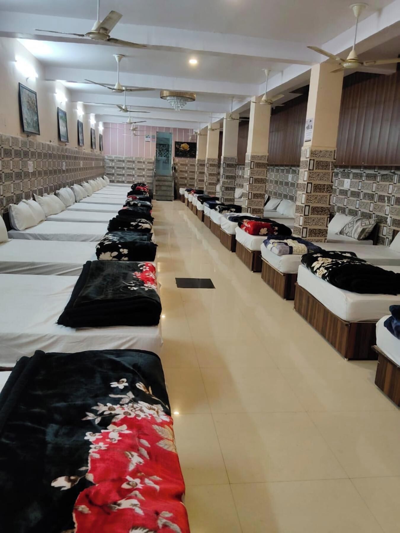 Una camera d'albergo con letti disposti in file, ciascuno con cuscino e coperta.