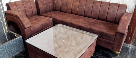 A brown leather sectional sofa with a glass-top coffee table in a room with a marble floor and patterned wallpaper.