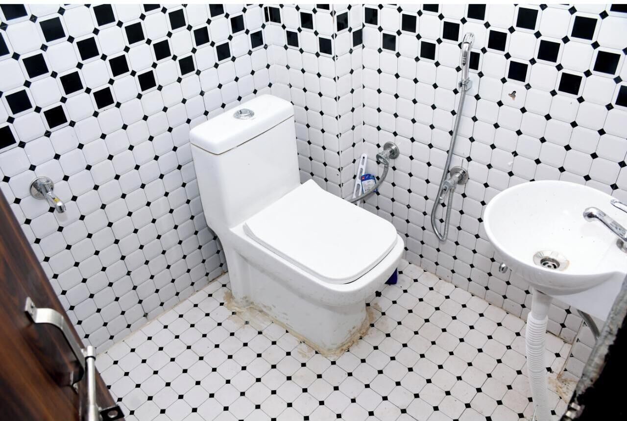 Un baño con inodoro blanco, lavamanos y ducha. El piso está cubierto de baldosas con un estampado blanco y negro.