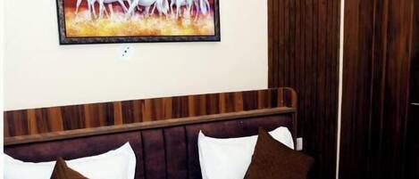 Una habitación de hotel con cabecera de madera, ropa de cama blanca, almohadas marrones y una manta marrón. En la pared, un cuadro de caballos blancos.