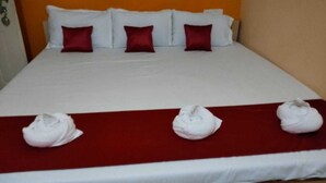 A hotel room with a bed, white bedding, red pillows, and three towels placed on a red bed runner. - AG Residency (Port Blair)