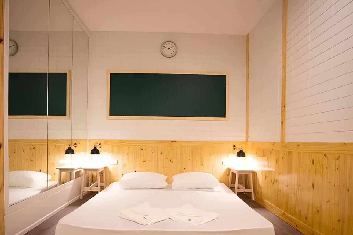 A hotel room with a large bed, two bedside tables with lamps, a mirror, a clock on the wall, and wooden paneling.