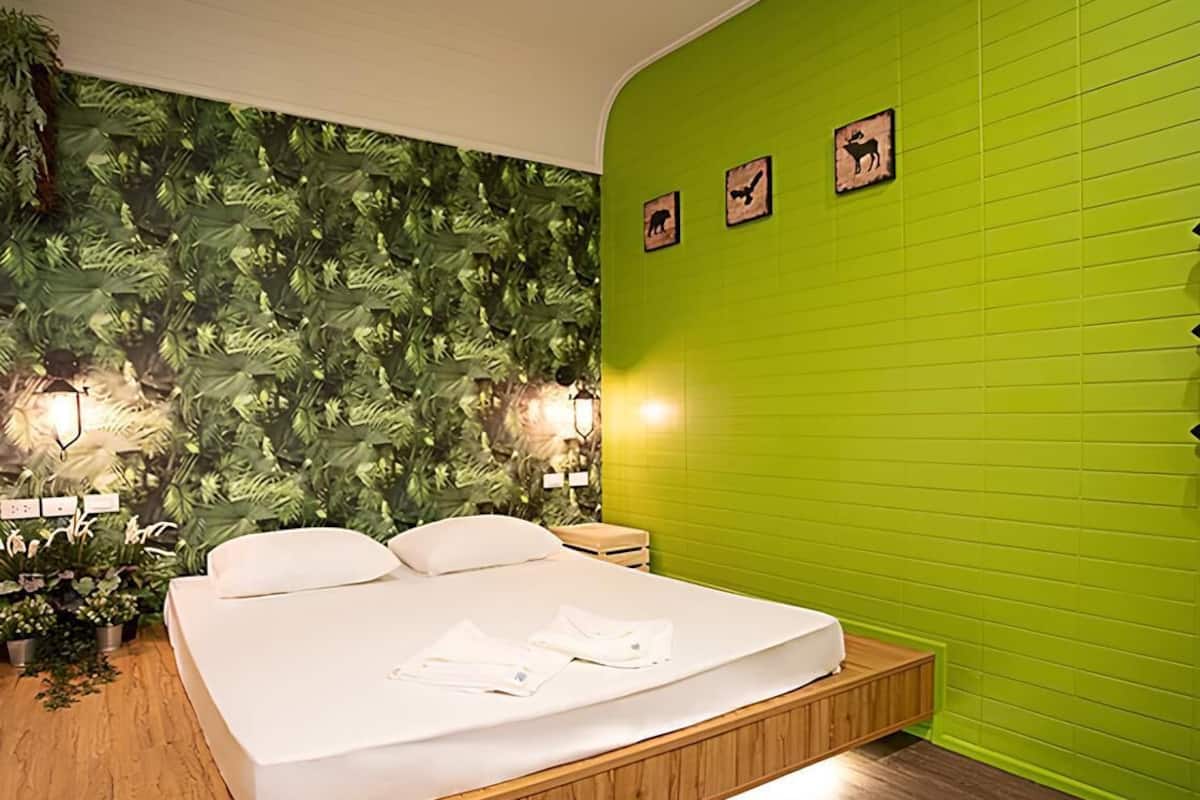 A modern bedroom with a bed, green walls, and a wall-mounted plant.