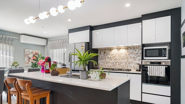 Een moderne keuken met witte kasten, een centraal eiland met barkrukken, een magnetron en een fornuis.