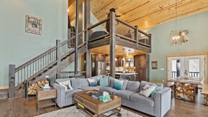 A spacious living room with a gray sectional sofa, a wooden coffee table, and a staircase leading to an upper level. - Alaskan Moose Lodge | Yellowstone + Hot Tub, Fire Pit & AC (Island Park)