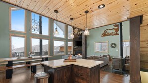 A spacious kitchen with a large island, wooden ceiling, and large windows offering views of the outdoors. - Alaskan Moose Lodge | Yellowstone + Hot Tub, Fire Pit & AC (Island Park)