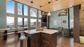 A spacious kitchen with a large island, wooden ceiling, and large windows offering views of the outdoors.