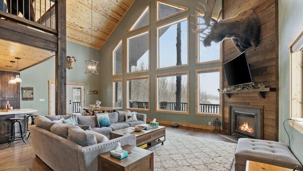 A spacious living room with a large sectional sofa, a fireplace, and a mounted deer head. - Alaskan Moose Lodge | Yellowstone + Hot Tub, Fire Pit & AC (Island Park)