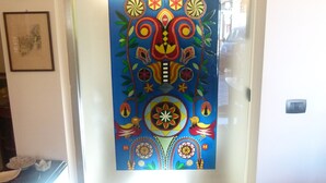 Un couloir orné d’une œuvre d’art abstraite aux couleurs vives sur le mur, avec un tableau encadré sur la gauche et un sol carrelé.