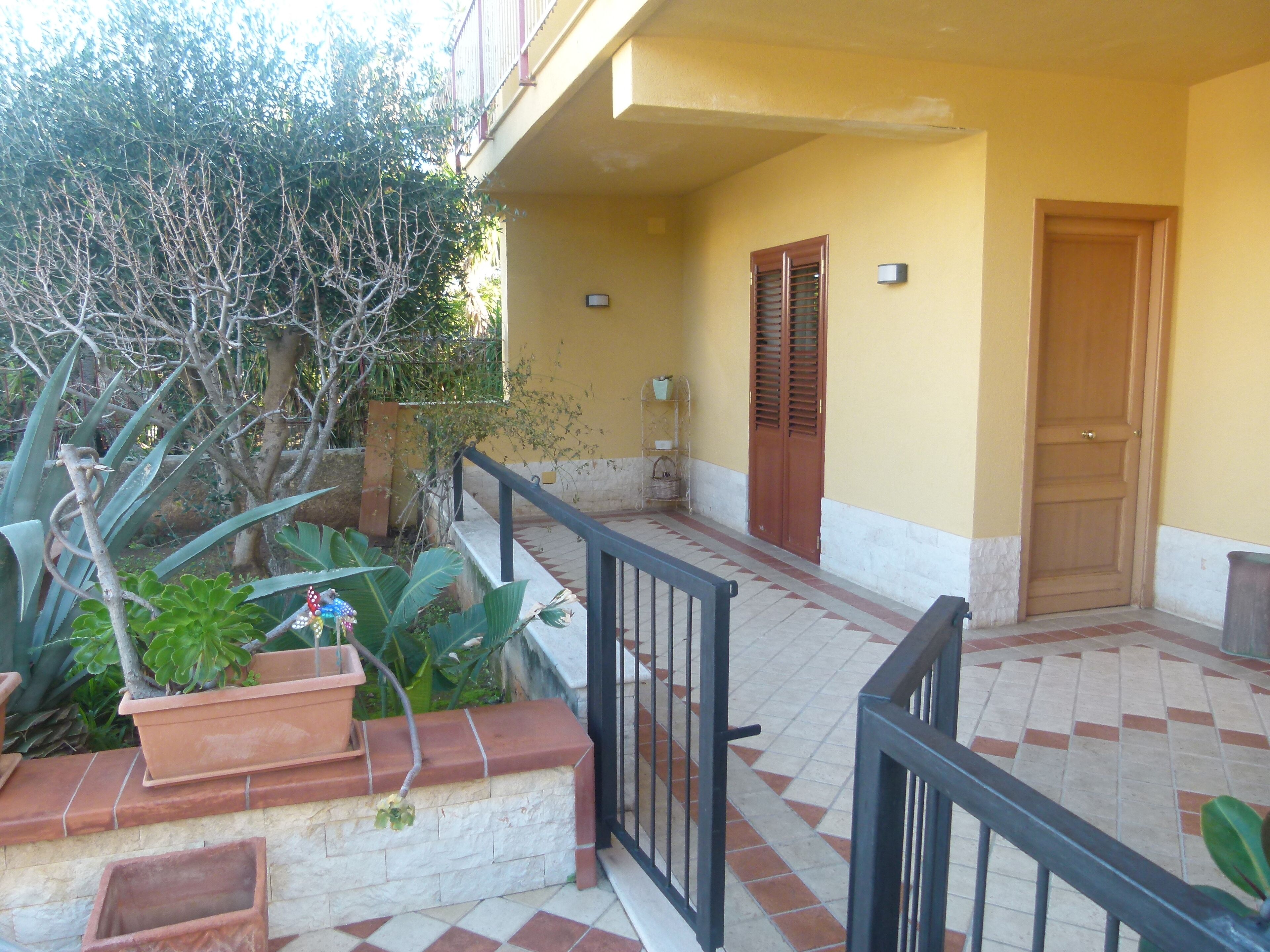 A balcony with terracotta planters, a wooden door, and a tiled floor.