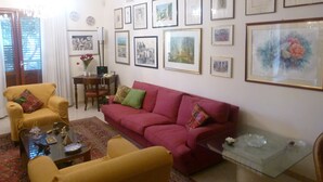 Un salon avec un canapé rouge, des fauteuils jaunes, une table basse en verre et un coin repas comprenant une table et des chaises.