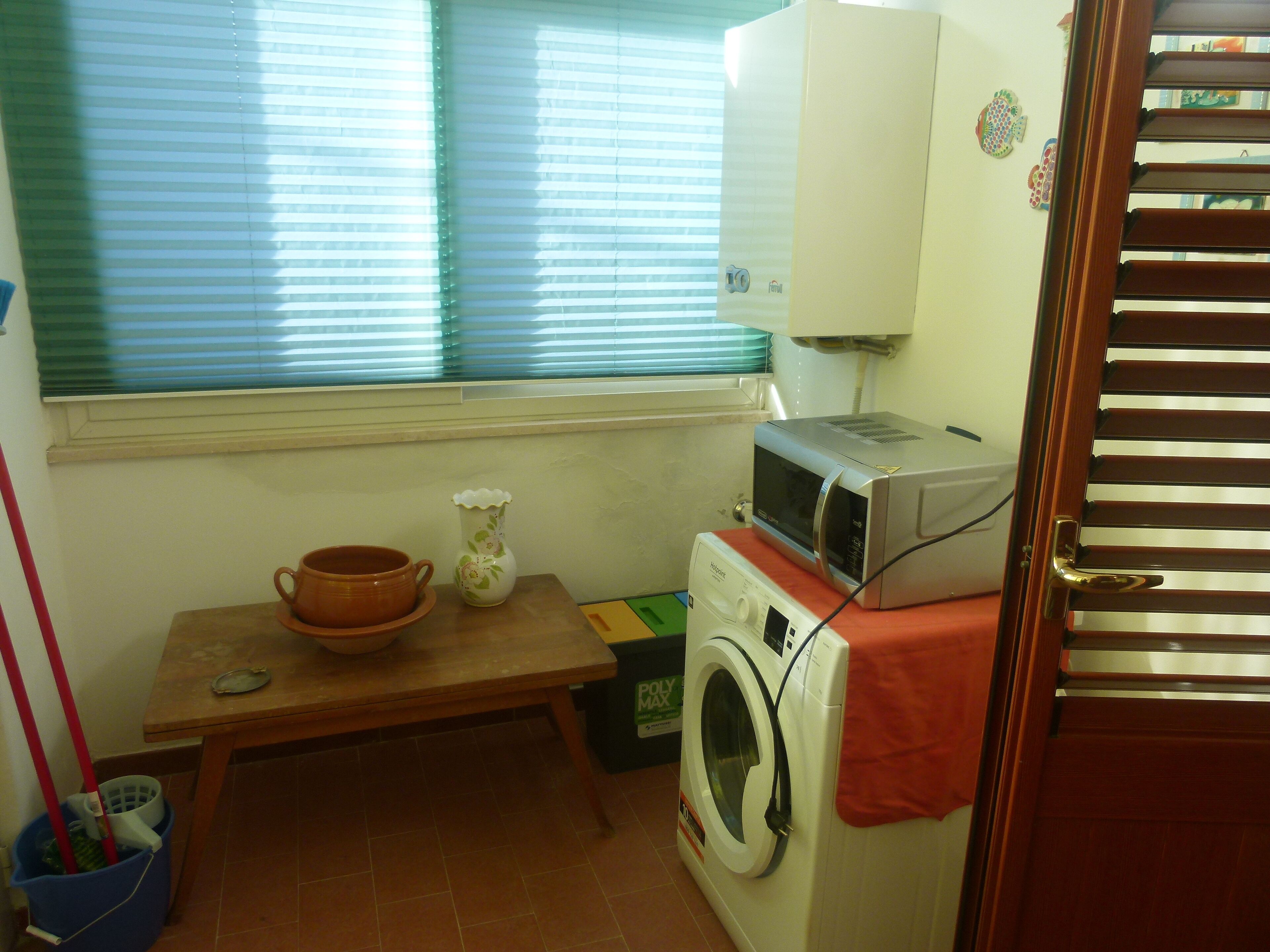 Un espace buanderie comprenant un lave-linge, un four à micro-ondes, une table avec une théière et une fenêtre avec des stores.