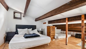 Ein Schlafzimmer mit einem Bett, Holzbalken, einem Schminktisch und einem kleinen Fenster.