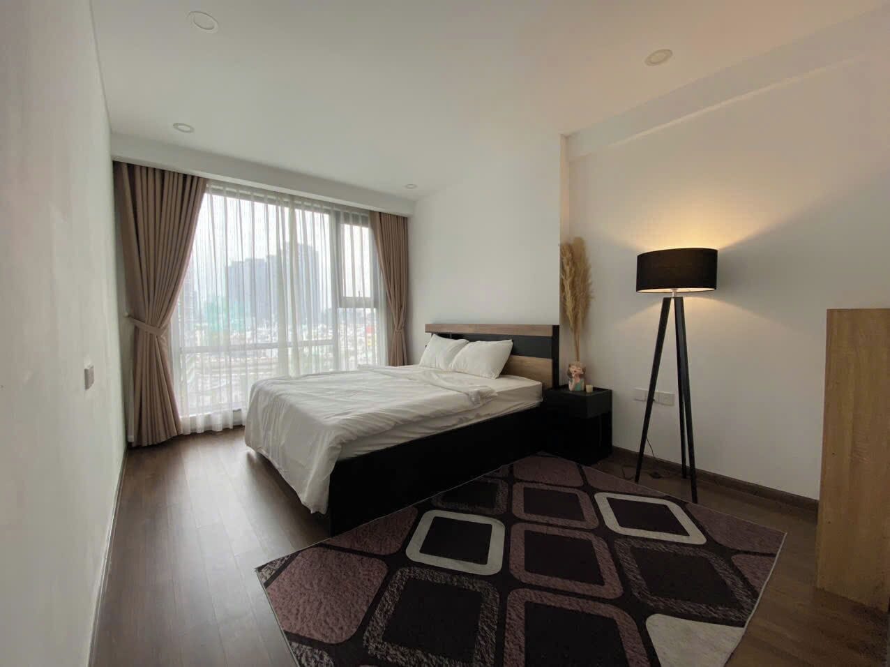 Una camera d'albergo moderna con un letto grande, una lampada da terra e vista sulla città dalla finestra.