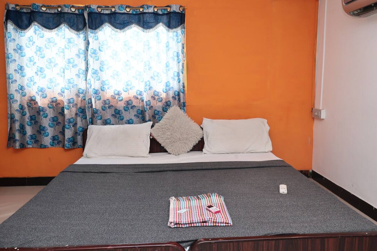 Una cama con un colchón gris, almohadas blancas y un edredón mullido. Una manta a cuadros está doblada al pie de la cama.