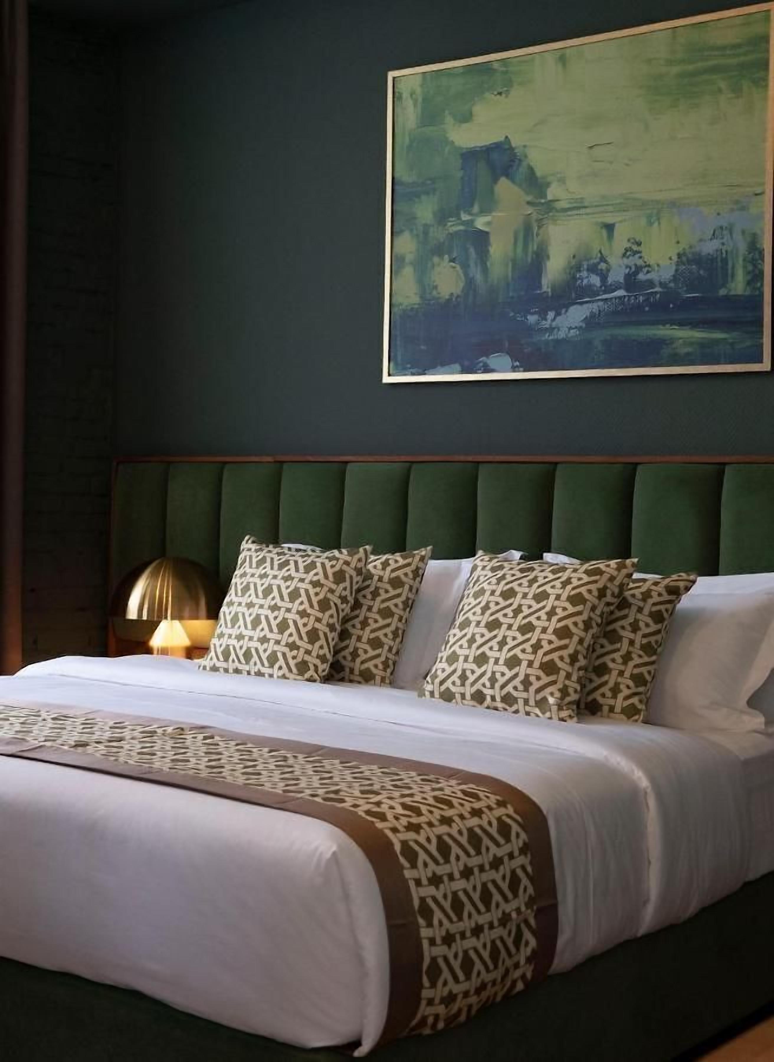 Un lit bien fait, agrémenté d’oreillers à motifs et d’une tête de lit recouverte d’un tissu vert.