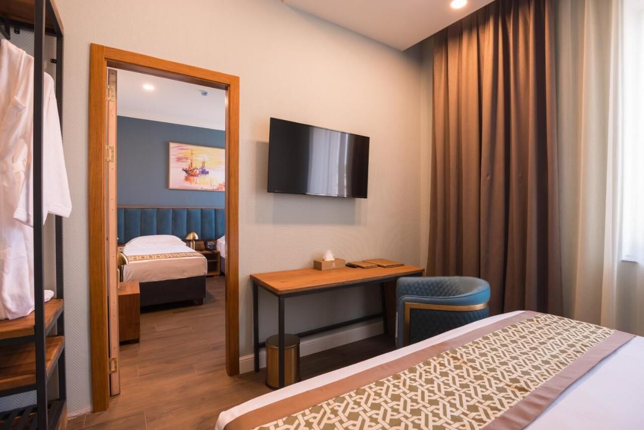 A hotel room with a bed, a desk, a chair, a TV, and a painting on the wall.