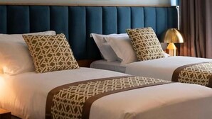 Una camera d'albergo con due letti, un quadro grande appeso al muro e una lampada sul comodino.