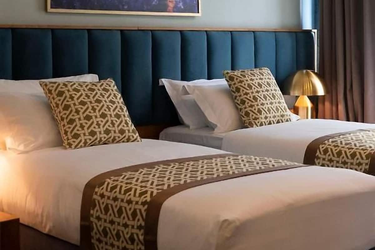 Ein Hotelzimmer mit zwei Betten, einem großen Gemälde an der Wand und einer Lampe auf dem Nachttisch.