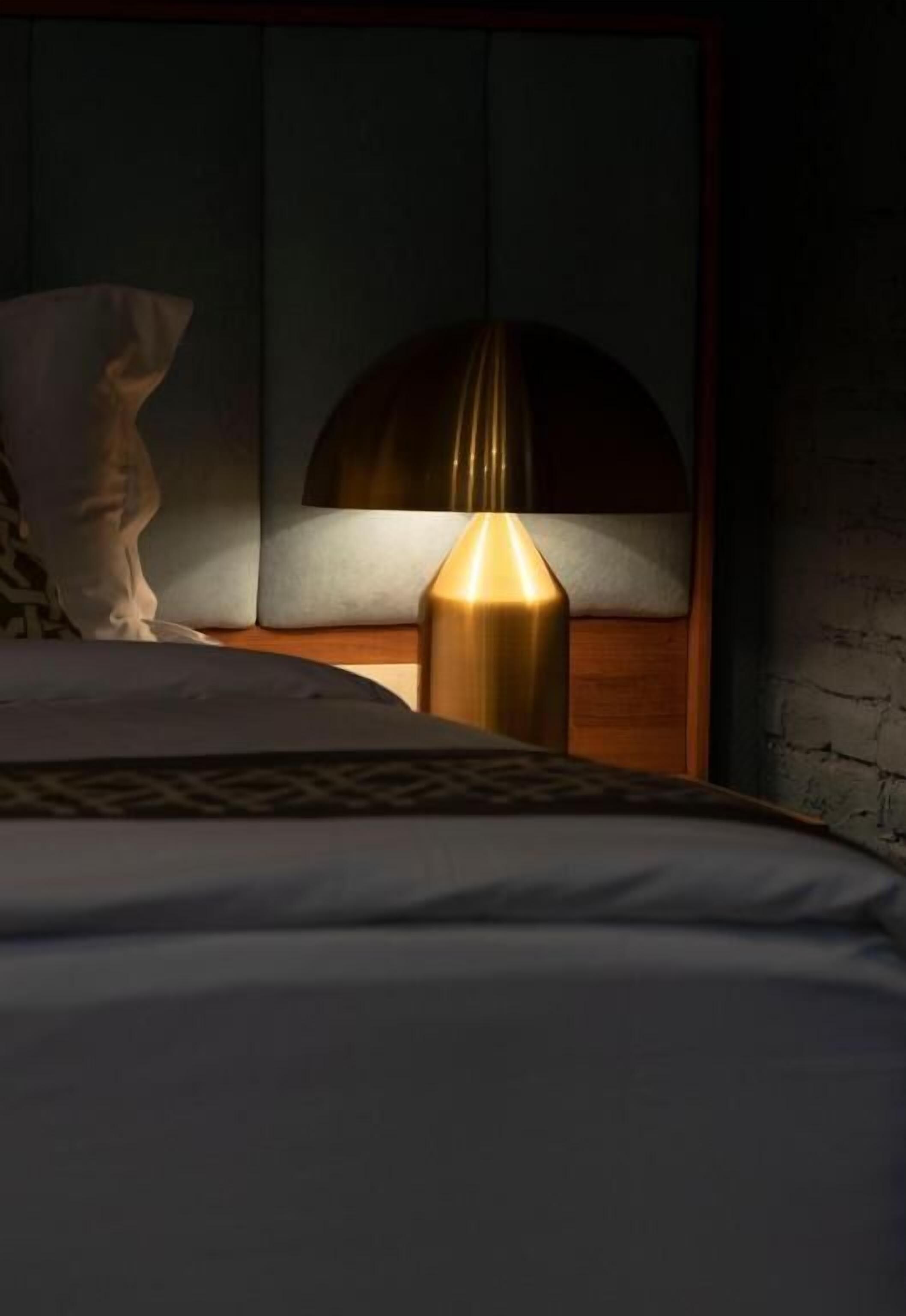 Una cama bien tendida con una colcha estampada, una lámpara de noche y una almohada decorativa en una mesita de noche.