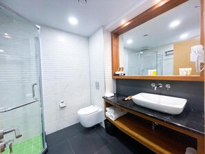 A modern bathroom with a glass shower enclosure, a white toilet, a large mirror, and a black countertop with a white sink.
