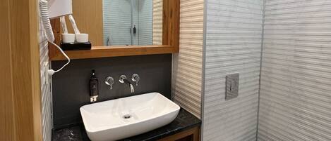 Un baño moderno con un lavamanos blanco, tocador de madera y un inodoro.