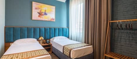 Habitación de hotel con dos camas, un cuadro en la pared, cabecera de madera, mesita de noche, lámpara y perchero.