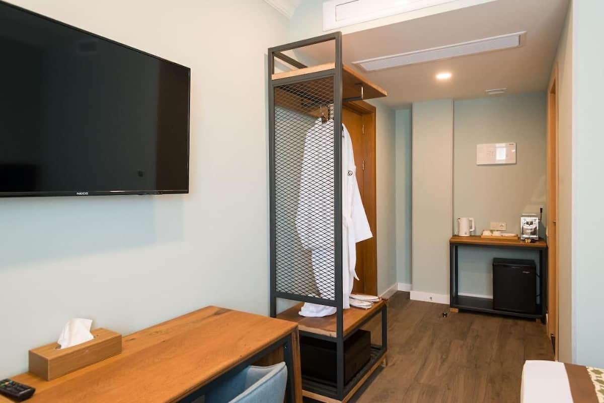 Ein Hotelzimmer mit Fernseher, einem Holztisch mit Fernbedienung, einer kleinen Küchenzeile und einer Duschkabine.