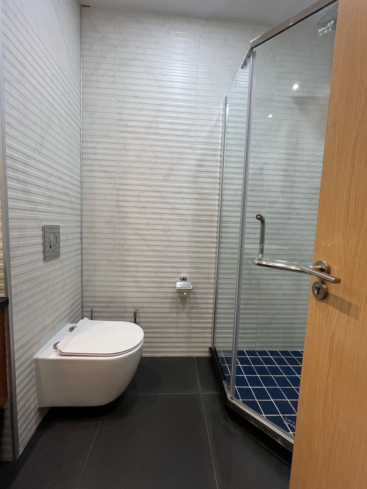 Une salle de bain moderne avec des toilettes, une douche à parois de verre et un carrelage au sol.