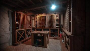 A wine cellar with wooden racks and tables, featuring a brick floor and exposed wooden beams.