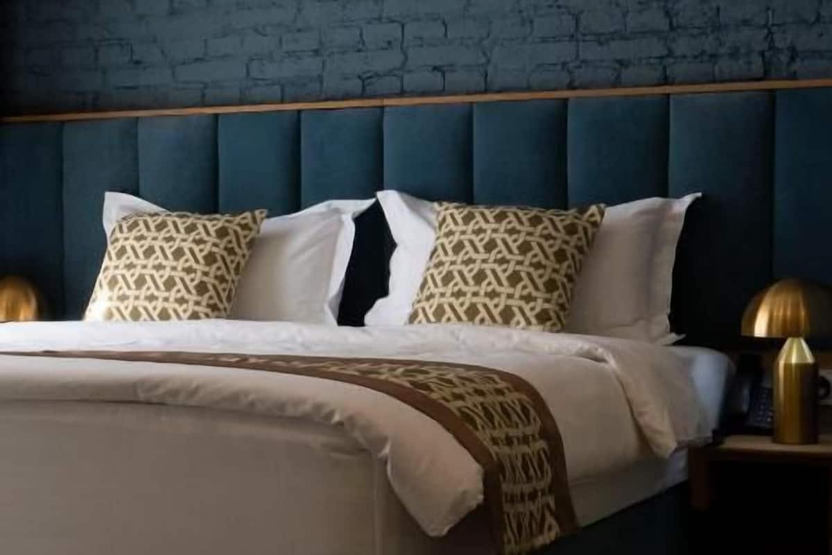 Ein Bett mit blauem Kopfteil, weißer Bettwäsche und gemusterten Kissen.