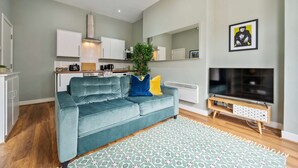 A modern living room with a teal sofa, a patterned rug, a flat-screen TV, and a kitchen area with white cabinets and a microwave. - Host Stay The Georgian Quarters at Bedford II and III (Liverpool)