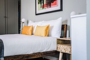 A neatly made bed with white and yellow pillows, a wooden headboard, and a bedside table with a lamp.