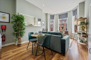 Een moderne woonkamer met een groene bank, een ronde houten tafel en een plant in pot.