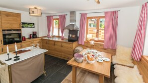 A modern kitchen with wooden cabinets, a central island, and a dining area with a table set for breakfast. - Vacation apartment Rehkitz (Reit im Winkl)