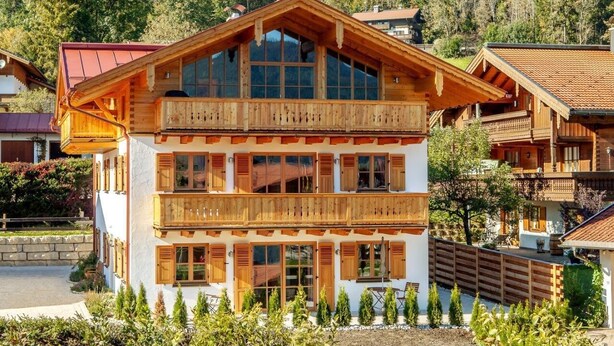 A two-story wooden chalet with balconies, surrounded by a forested landscape. - Vacation apartment Rehkitz (Reit im Winkl)