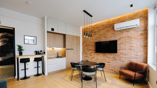 A modern kitchen with a brick wall, a flat-screen TV, and a dining area with a table and chairs. - G Residence - Luxe 1-bed, smart home on Ermou (Athina)