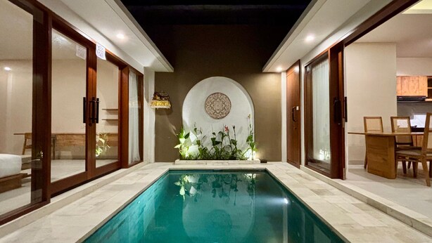 Una piscina con suelo de baldosas, rodeada de puertas y paredes de madera, con un muro decorativo circular al fondo.