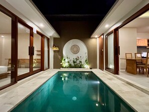 A swimming pool with a tiled floor, surrounded by wooden doors and walls, with a circular decorative wall in the background. - Solvana Villas Sanur by AGATA (Denpasar)