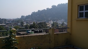 A balcony with a tiled floor, potted plants, and a view of a cityscape with buildings and trees. - Kalita Boarding Home (Guwahati)