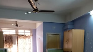 A room with two single beds, a wooden wardrobe, a ceiling fan, and a window with curtains. - Kalita Boarding Home (Guwahati)