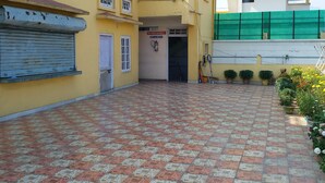 A yellow building with a tiled courtyard, a closed shuttered door, and a green fence. - Kalita Boarding Home (Guwahati)