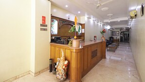 A hotel reception area with a wooden reception desk, a statue, and a flag. - Hotel Rossette (New Delhi)