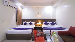 A hotel room with two beds, a small table with a tray of food and drinks, a red chair, and a ceiling fan. - Hotel Rossette (New Delhi)