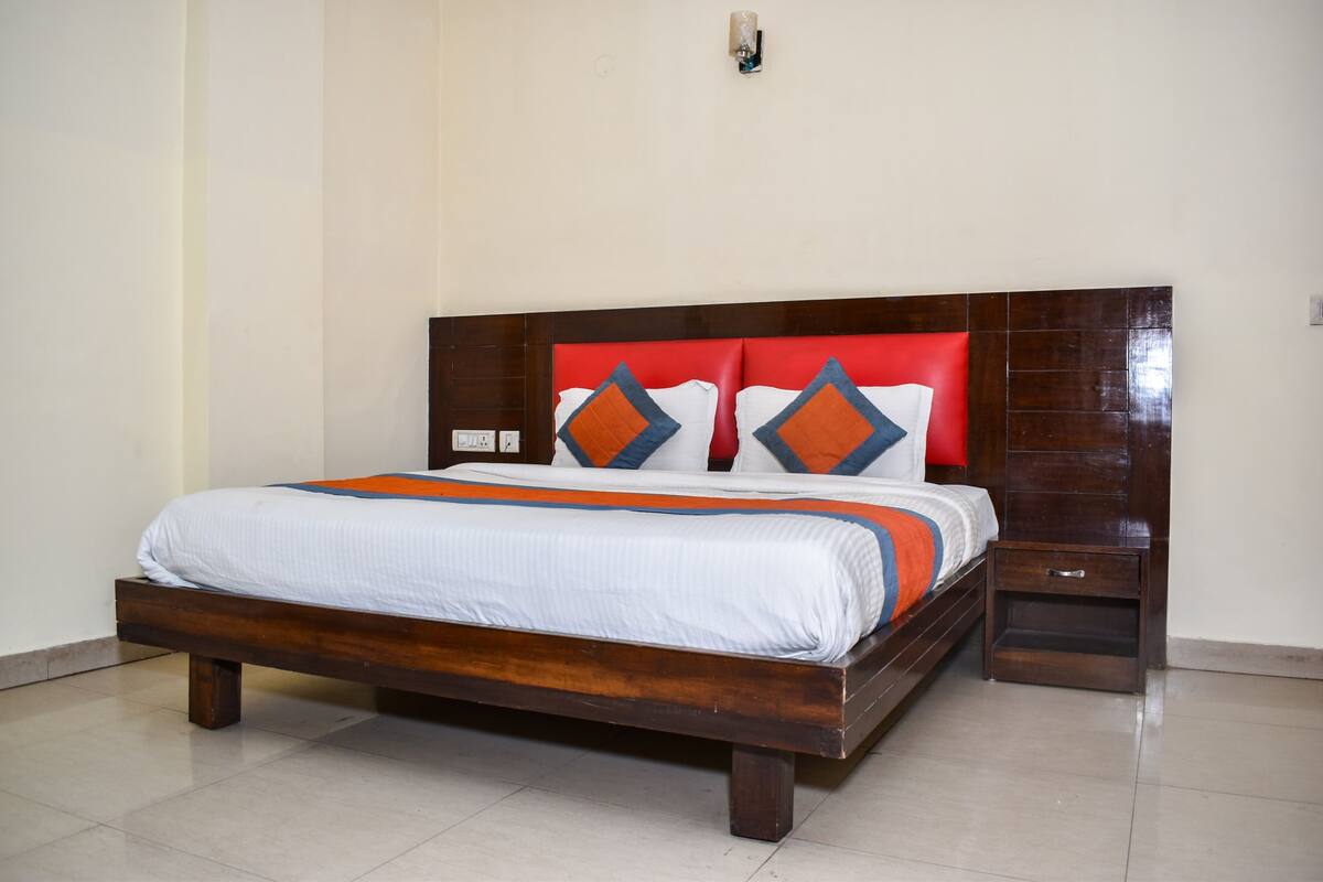Una cama con estructura de madera, cabecera roja y almohadas estampadas.
