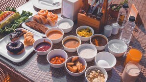 A breakfast spread on a wicker table with various dishes, including pastries, fruits, and beverages. - Hotel Rossette (New Delhi)