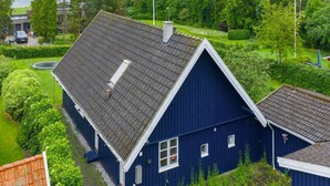 A blue house with a sloped roof, surrounded by lush greenery and a body of water in the background. - "Gravers" - 150m from the sea by Interhome (Svendborg)
