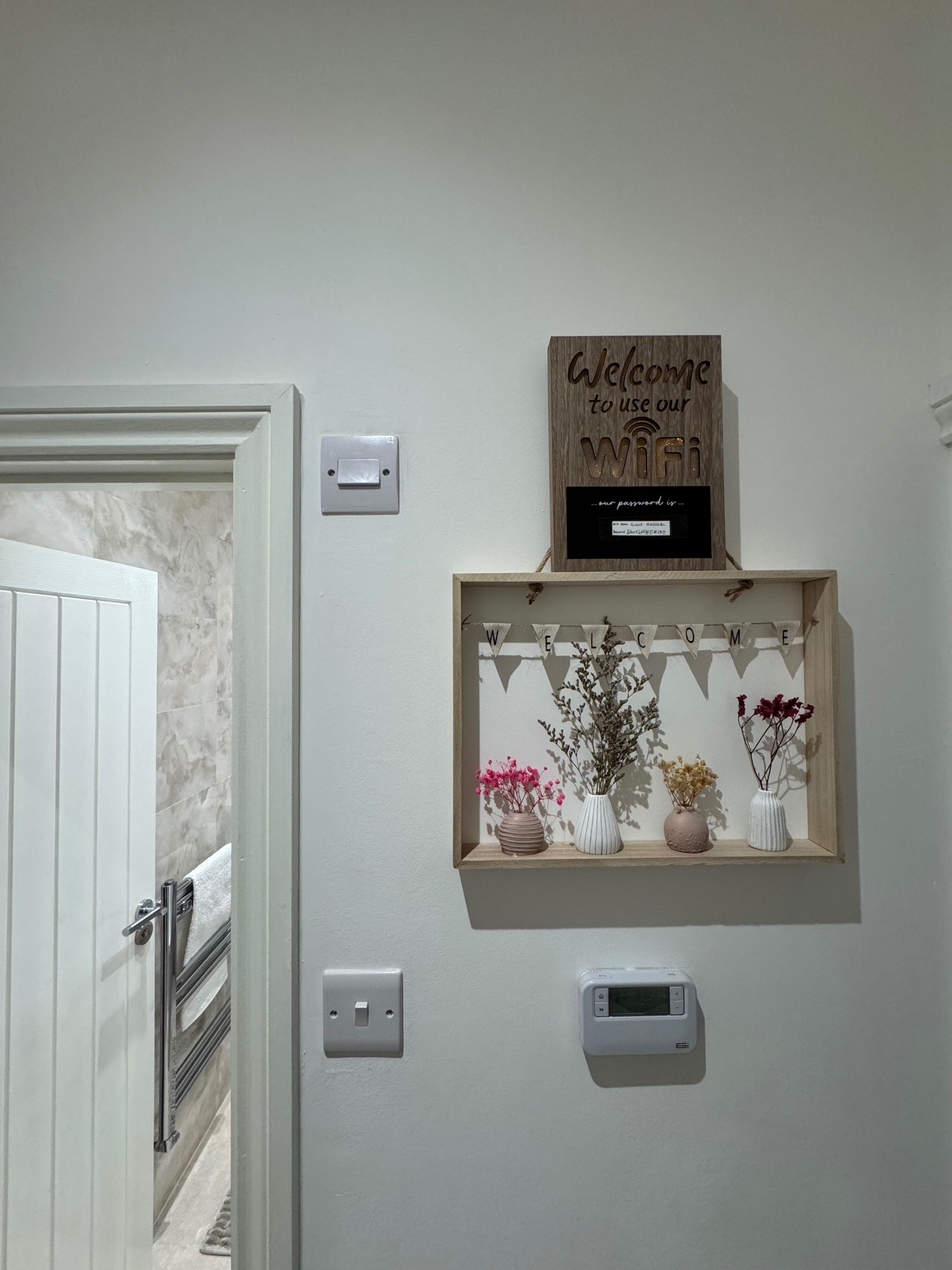 A wall-mounted shelf with a welcome sign and a thermostat.