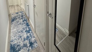 A hallway with a blue and white patterned rug, white walls, and a door with a black frame. - Cozy 2br-5guests-near Attractions-garden (London)