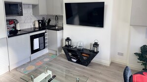 A modern kitchen with white cabinets, a black countertop, and a large flat-screen TV mounted on the wall. - Cozy 2br-5guests-near Attractions-garden (London)